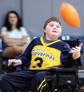Young boy wearing a jersey and in a motorized wheelchair tosses a football